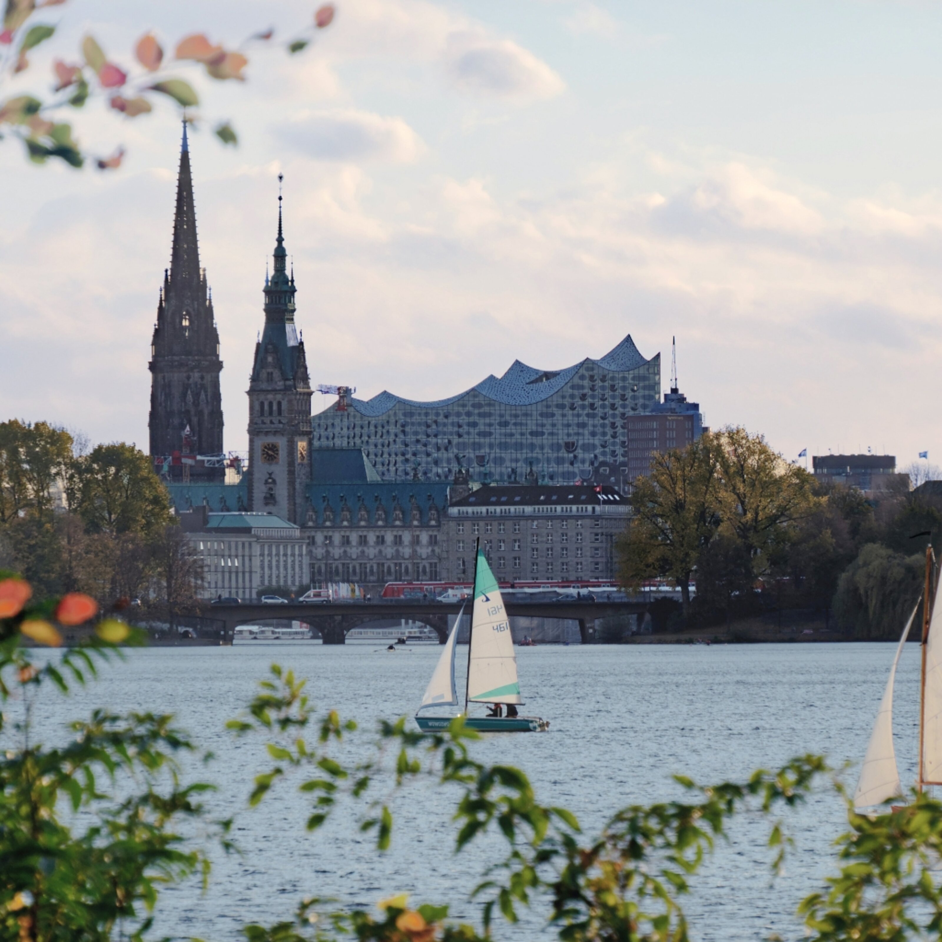 View of Hamburg’s iconic Elbphilharmonie and St. Nikolai Church with sailboats on Alster Lake, near MEININGER Hotel Hamburg City Center.