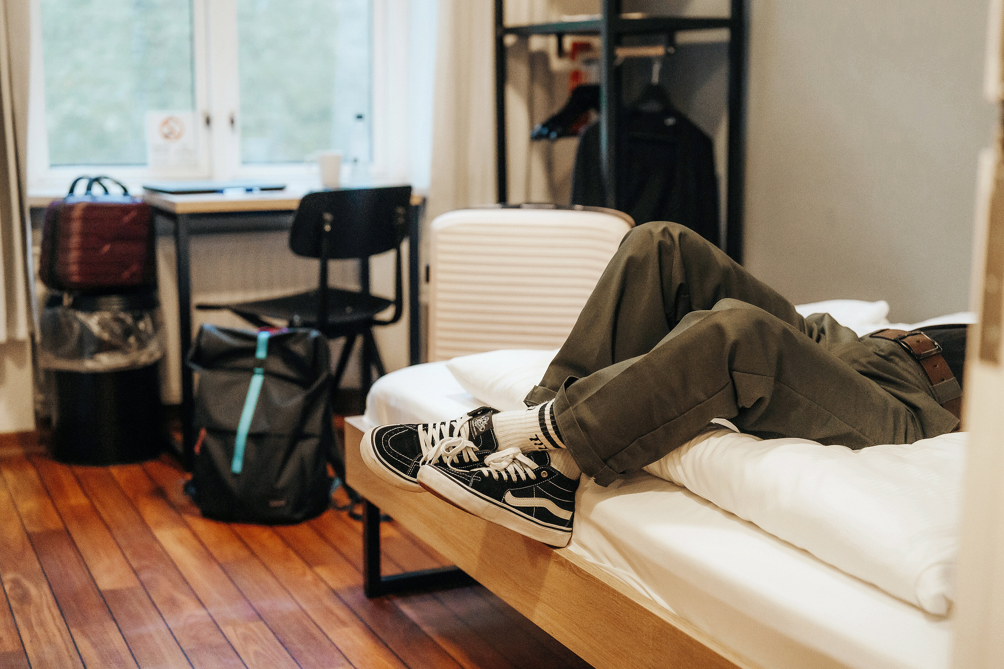 Gambe distese in camera con zaino, scrivania e armadio in vista