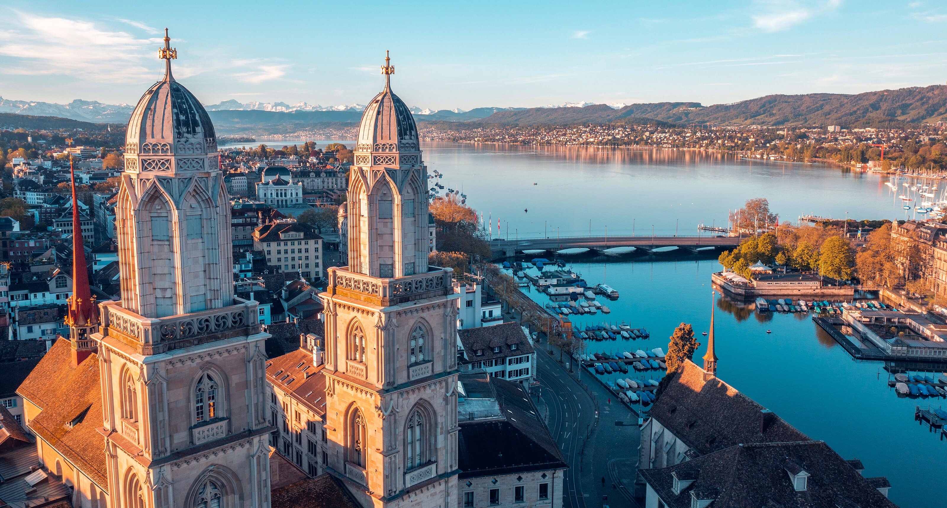 Panoramic view of Grossmünster, Lake Zurich, and Alps near MEININGER Hotels in Switzerland.